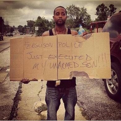 Michael Brown's stepfather holds a sign which reads, &quot;Ferguson Police Just Executed My Unarmed Son!!!&quot;